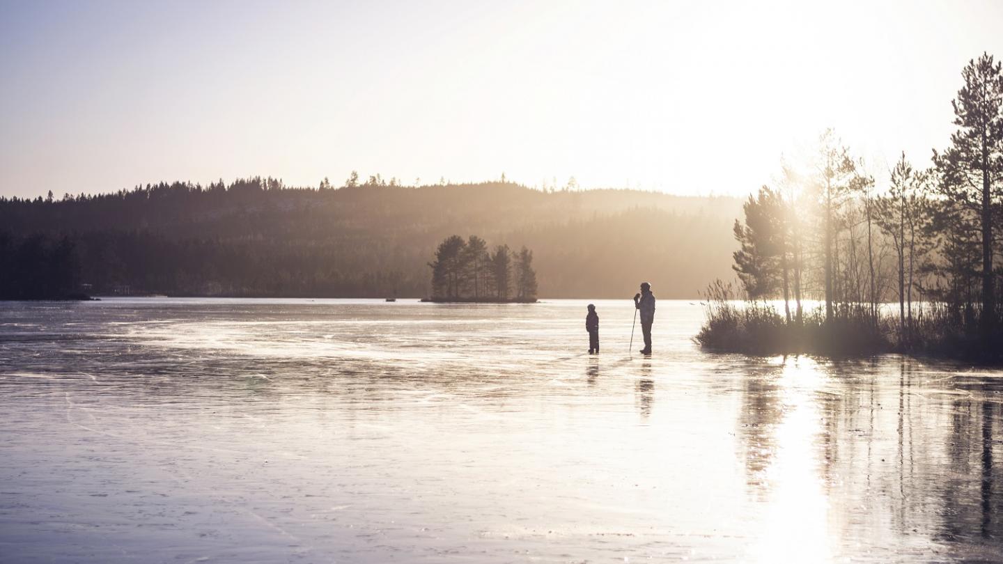 Een volwassene en een kind op het ijs met de zon op de achtergrond.