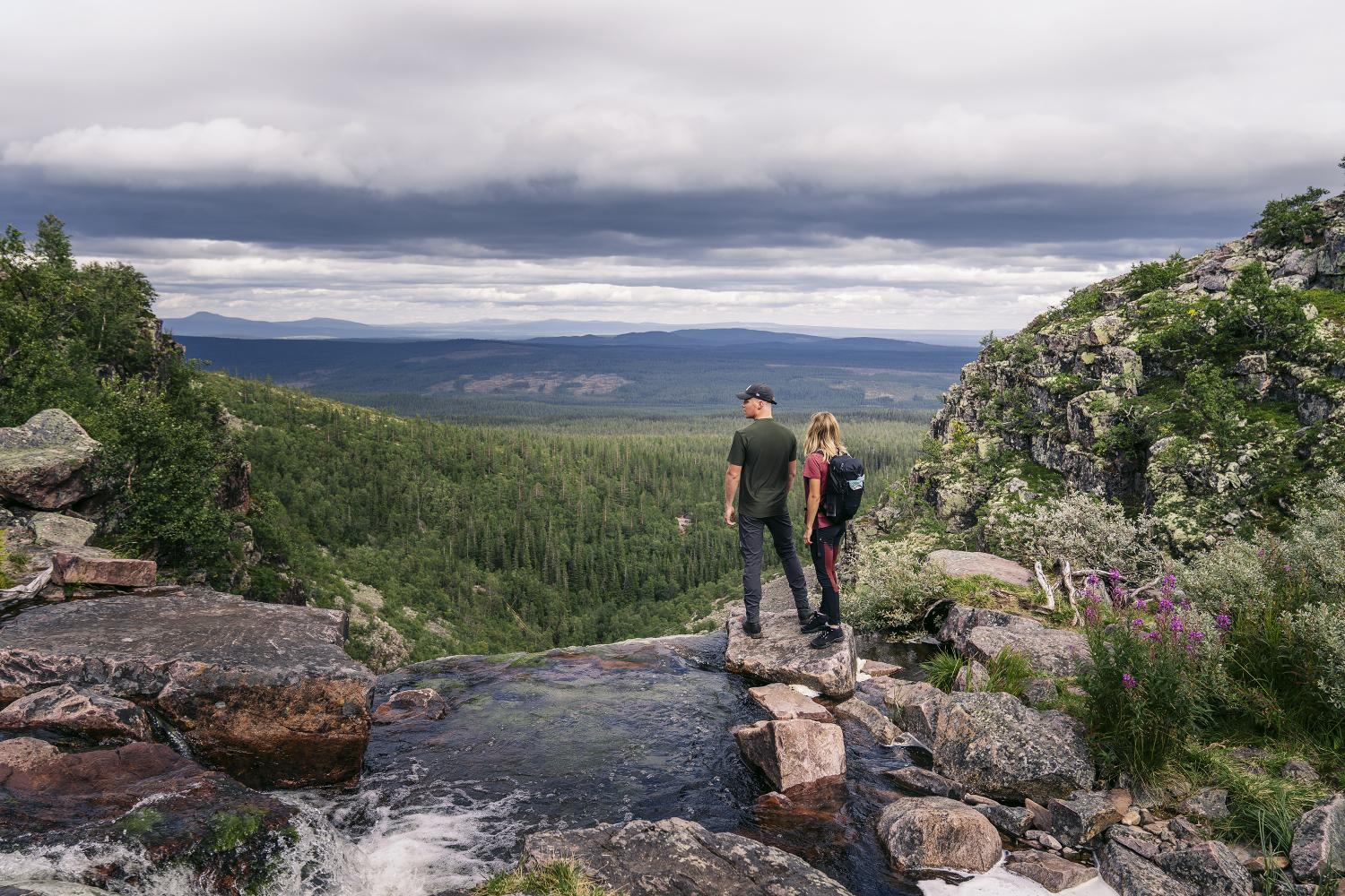 Ett ungt par står på toppen av et fossefall i Fulufjället og titter på utsikten.