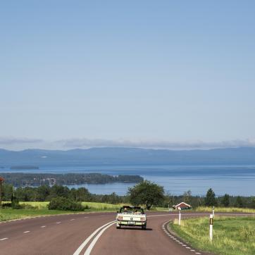 Een oude auto rijdt over de weg met uitzicht op het Siljanmeer.