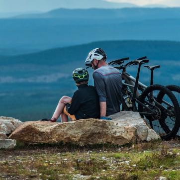 Far og sønn sitter på et fjell med MTB-syklene sine.