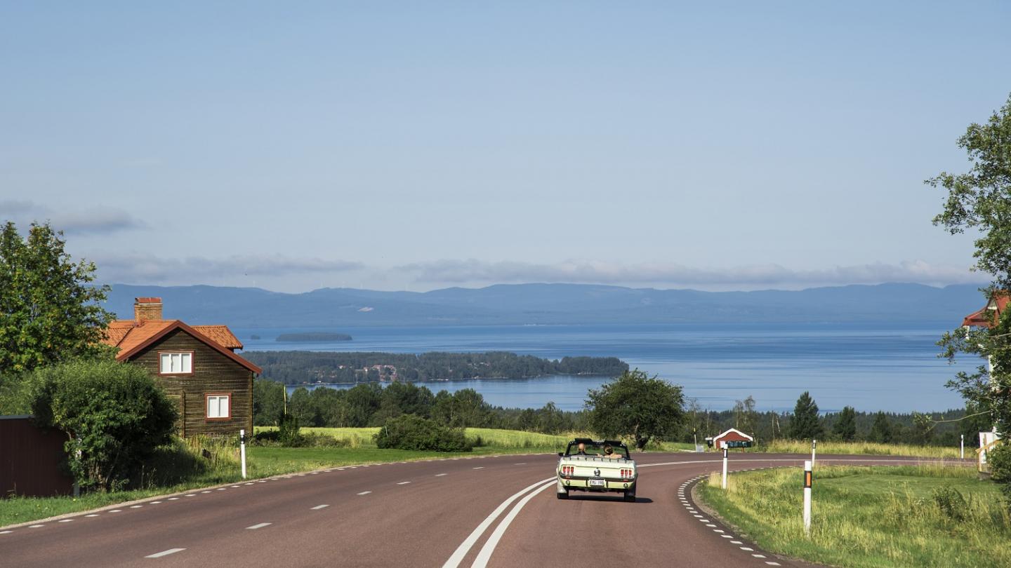 Een oude auto rijdt over de weg met uitzicht op het Siljanmeer.