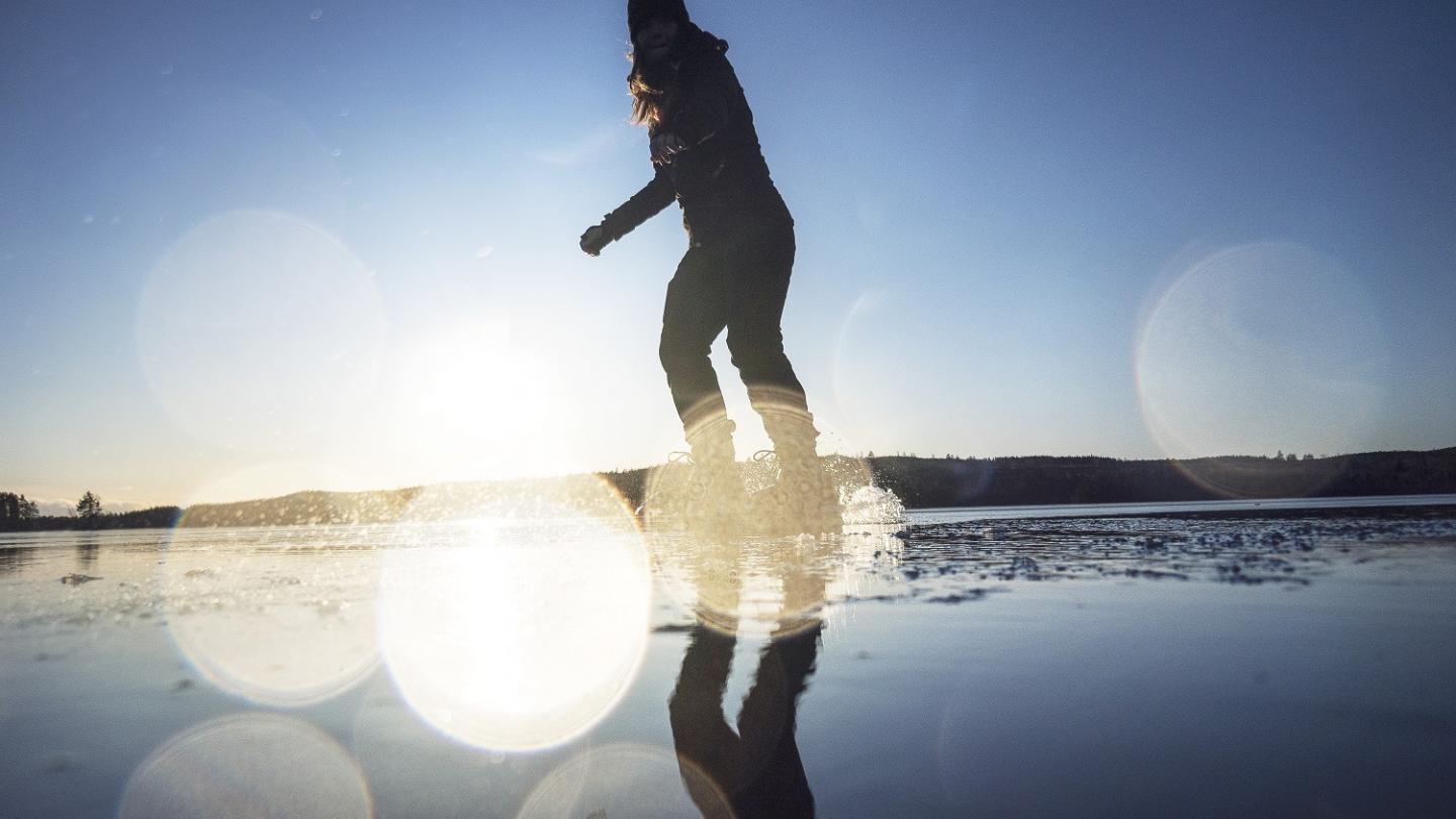 Een vrouw op schaatsen op een baan met weerspiegelingen van de zon.
